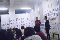Two teacher talking in front of a wall on which Latin letters have been pinned